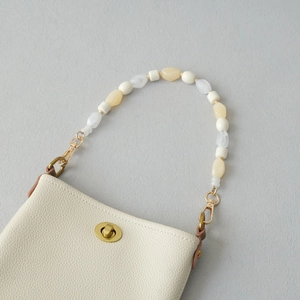 Détail de la poignée en perles amovible sur un sac en cuir beige avec fermoir doré