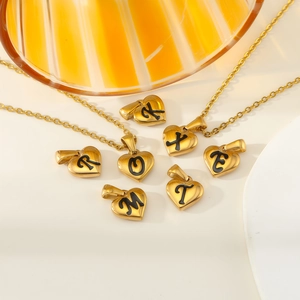 Détail de pendentifs coeur dorés avec lettres en émail noir sur fond décoratif