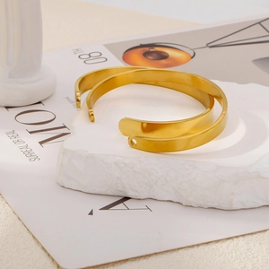 Detail of polished gold stainless steel open bangles with circular hole on textured stone