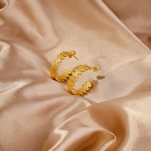 Close-up of gold C-shaped leaf texture earrings on a champagne satin background