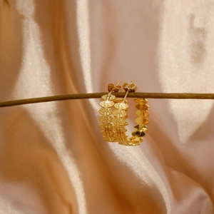 Detail of gold leaf textured C-shaped stainless steel earrings on a satin background