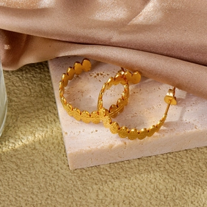 Close-up of golden textured leaf-style hoop earrings on a soft pink stone tray