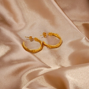 Dettaglio di orecchini a cerchio in bambù placcati oro 18k su sfondo di seta champagne