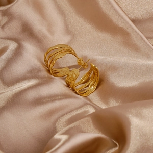 Macro dettagliata di orecchini geometrici dorati su un elegante tessuto di seta champagne