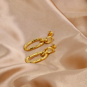 Detailed close-up of golden U-shaped link earrings with lava texture on champagne silk