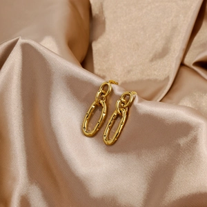 Detailed close-up of golden double-layer oval earrings on luxury champagne silk background