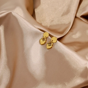 Gros plan de boucles d'oreilles cœur dorées sur un élégant tissu de soie champagne