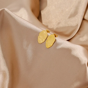 Close-up of golden irregular textured leaf earrings on elegant champagne silk fabric