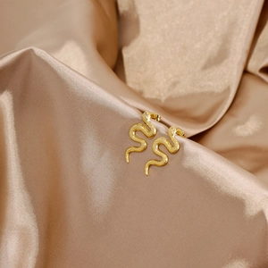 Detailed close-up of 18k gold snake-shaped earrings on elegant champagne silk fabric