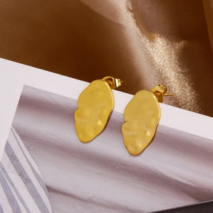 Detail of gold lava texture irregular leaf earrings on a white card with satin background