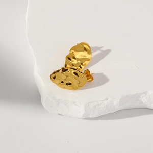 Detailed macro view of gold irregular lava texture leaf earrings on a stone base