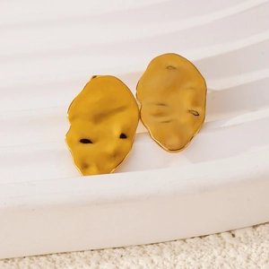 Macro detail of gold lava-textured leaf earrings on a minimalist display stand