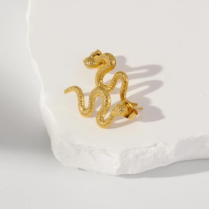 Macro shot of gold snake earrings with detailed scale texture on white stone surface