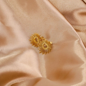 Nahaufnahme goldener Vintage-Herz-Ohrringe auf elegantem champagnerfarbenem Seidenstoff