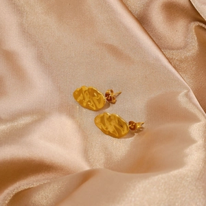 Detail of golden leaf earrings with hammered lava texture on champagne satin fabric
