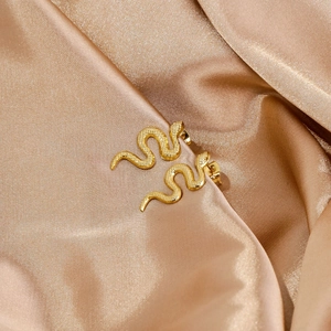 Close-up of golden snake stud earrings with realistic scale texture on champagne silk fabric