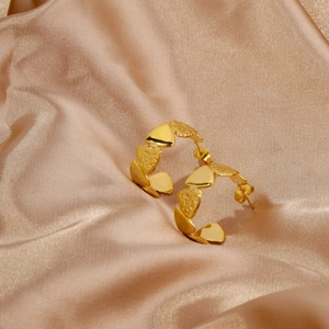 Detail of C-shaped golden earrings with textured heart charms on champagne satin cloth