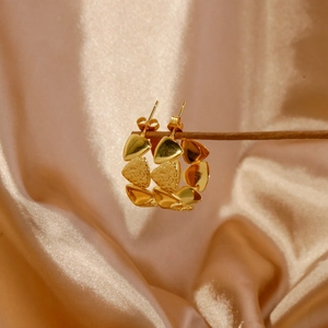 Detail view of gold triangular geometric hoop earrings on a silk velvet background