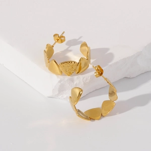 Macro shot of gold-plated clover earrings with hammered texture on white stone base
