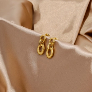 Detail of interlocking gold chain link earrings on a champagne silk fabric background