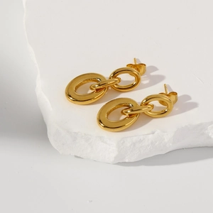 Detailed view of glossy interlocking gold oval earrings on a minimalist white stone pedestal