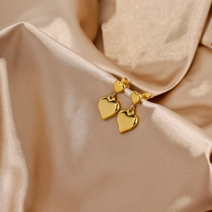Détail de boucles d'oreilles cœur dorées polies sur un tissu en satin de soie champagne