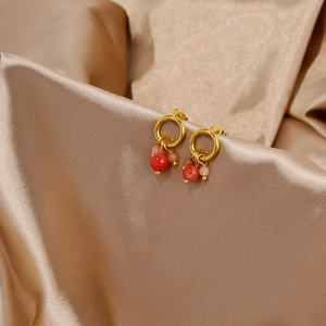 Dettaglio di orecchini in oro 18k con pendenti a perla rossi e rosa su raso champagne