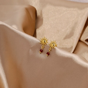 Orecchini a girasole dorati con rubino rosso su elegante sfondo in seta color champagne
