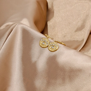 Detail of 18k gold evil eye earrings with zircon inlay on luxury silk fabric