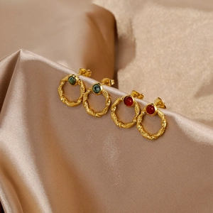 Detail of 18k gold twist earrings with emerald and red agate stones on satin fabric