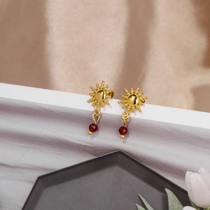 Dettaglio ravvicinato di orecchini a girasole con pendente rosso rubino e finitura oro