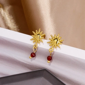 Dettaglio di orecchini a girasole dorati con perle rosso rubino su elegante raso champagne
