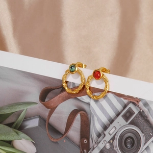Close-up of 18k gold earrings with emerald green and ruby red stones on silk