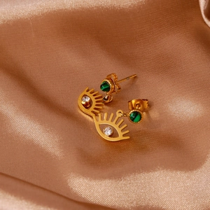 Dettaglio degli orecchini Evil Eye dorati con pietra verde smeraldo su seta champagne