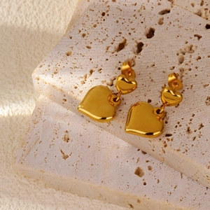 Détail des boucles d'oreilles double cœur doré sur un plateau en pierre naturelle