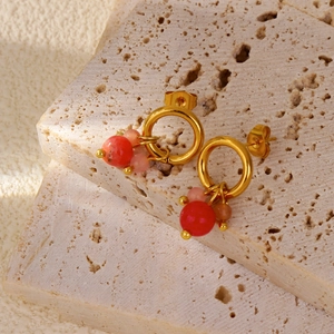 Dettaglio degli orecchini in oro 18k con perline rosse e rosa su pietra travertino
