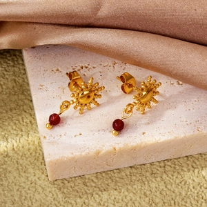 Dettaglio ravvicinato di orecchini a girasole dorati con perle di rubino rosso su marmo