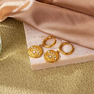 Detail of 18k gold evil eye earrings featuring white zircon inlay on marble and satin background