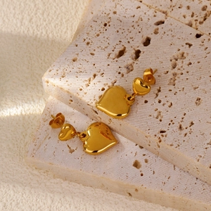 Vue détaillée de boucles d'oreilles double cœur doré sur une surface en pierre de travertin