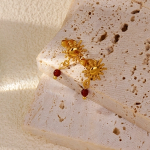 Primo piano di orecchini a girasole dorati con perline rosse su pietra beige