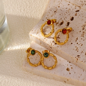 Macro detail of 18k gold twist hoop earrings with emerald green and red stones