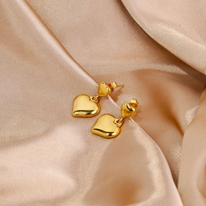 Détail de boucles d'oreilles doubles cœurs dorés sur fond de tissu en soie champagne