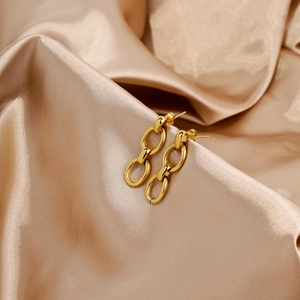Détail macro de boucles d'oreilles dorées à trois maillons sur fond de satin champagne