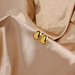 Macro view of minimalist polished gold rectangular stud earrings on silk fabric background