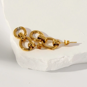 Détail de boucles d'oreilles dorées à double maillon sur un socle en pierre minimaliste