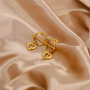 Detailed macro view of gold heart-shaped earrings on elegant champagne silk fabric texture