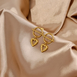 Close-up of golden heart earrings with hammered texture on elegant satin fabric background