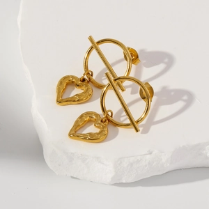 Detailed close-up of golden heart earrings with hammered texture on a stone stand