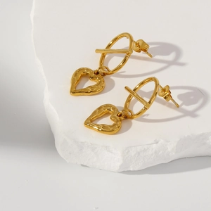 Macro detail of gold textured heart earrings displayed on a minimalist plaster block