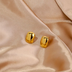 Detail of high-polished gold cube stud earrings on champagne satin background